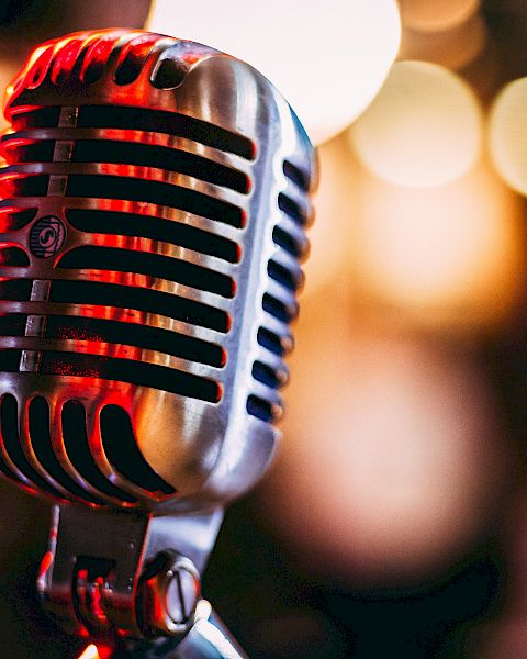 A close-up photo of a vintage-style microphone with colorful bokeh lights in the background, creating a warm and nostalgic atmosphere.