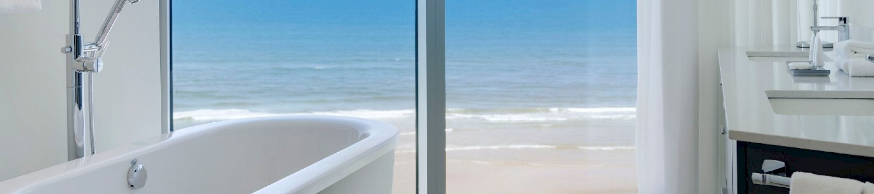 A bathroom with a freestanding tub and a large window overlooking the ocean. Text reads 