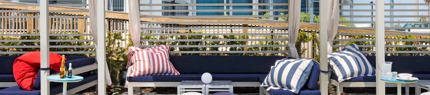 The image shows a modern outdoor cabana setup with seating and colorful cushions next to a building, with the text 